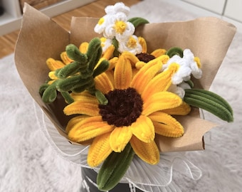 May include: A bouquet of pipe cleaner sunflowers and white daisies with green stems wrapped in brown paper. The bouquet is placed in a black container featuring a white skeleton print and is accented with a white sheer ruffled trim at the base.