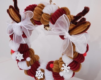 May include: A circular wreath crafted from brown, white, and deep red pipe cleaners. The wreath features two brown pipe cleaner antlers, two white sheer organza bows, three small white snowflake ornaments, and small red pom-poms.
