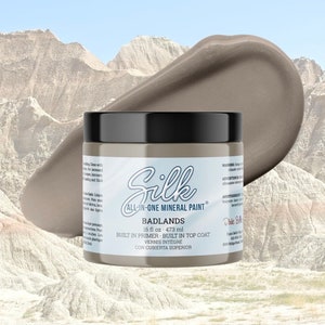 May include: A jar of "Silk" brand "Badlands" all-in-one mineral paint. The jar is light gray with a black lid. A swatch of the paint is next to the jar. The paint is 16 fl oz (473 ml).