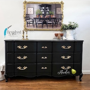 May include: A black dresser with gold hardware and a curved bottom. The dresser has nine drawers and is decorated with the word "Anchor".