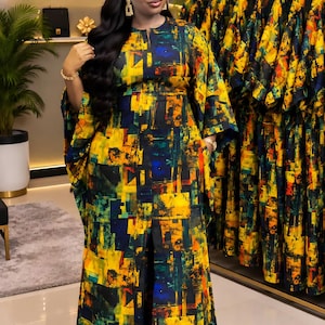 May include: A floor-length kaftan dress featuring a vibrant abstract geometric print in shades of yellow, navy blue, and green. The garment has a round neckline, wide kimono-style sleeves, and a central front slit that reveals matching trousers.