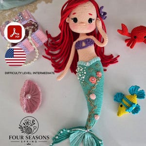 Peut inclure: Une poupée sirène crochetée avec de longs cheveux en laine rouge, un haut violet et une queue sarcelle ornée de petites fleurs roses et de perles blanches. Les accessoires incluent un coffre au trésor, un coquillage rose, un crabe et un poisson.