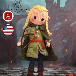 Op de afbeelding: Een gehaakte amigurumi-pop van een blonde elf met puntige oren, gekleed in een groene tuniek, een donkergroene mantel met een turquoise broche, een rode riem, een donkere broek en bruine laarzen, terwijl de pop een bruine boog vasthoudt.