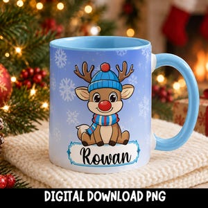 May include: A light blue ceramic mug featuring a cartoon reindeer wearing a blue knit hat and scarf, set against a light blue background with white snowflakes. The name Rowan is printed in black script inside a white rectangular label.