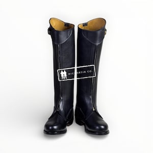 May include: A pair of black leather riding boots with front zippers and buckle details. The boots have a tall shaft and a rounded toe. The interior is a light tan color. The boots are displayed on a white background.