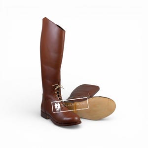 May include: A pair of brown leather riding boots. One boot is upright, showcasing the tall shaft and lace-up detail. The other boot lies on its side, revealing the sole. The boots have a classic equestrian design.