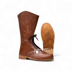 May include: Brown leather lace-up boots with a tall shaft. The boots have a classic design with a rounded toe and a sturdy sole. The second boot is shown with the sole facing up. The boots have the text "MICHARTIN CO."