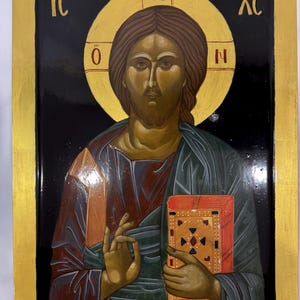 May include: A hand-painted icon of Jesus Christ with a gold halo and holding a book. The icon is on a black background with gold trim and the text "IC XC N" in gold.