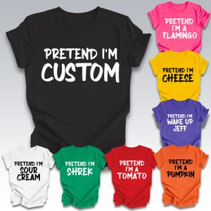May include: A collection of colorful t-shirts with the phrase "PRETEND I'M CUSTOM" in white on a black shirt. Other shirts include "PRETEND I'M A FLAMINGO", "CHEESE", "WAKE UP JEFF", "SOUR CREAM", "SHREK", "TOMATO", and "PUMPKIN".