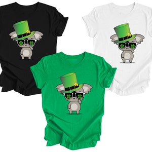 May include: Three t-shirts featuring a cartoon koala wearing a green leprechaun hat and sunglasses. The shirts are black, white, and green.