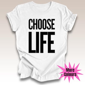 May include: White t-shirt featuring the text "CHOOSE LIFE" in large, bold, black capital letters. The shirt has a crew neck and short sleeves. A pink starburst graphic with "More Colours" is in the bottom right.
