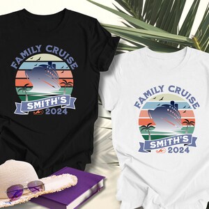 May include: Two t-shirts, one black and one white, with a "Family Cruise" design. The design features a cruise ship, palm trees, and the text "Smith's 2024" in a circular, retro style. A hat and book are in the foreground.