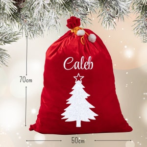 May include: A red Christmas gift bag, 70cm high and 50cm wide, with the name "Caleb" in white script. A white Christmas tree design is below the name. The bag is tied at the top with a red bow and white pom-poms.
