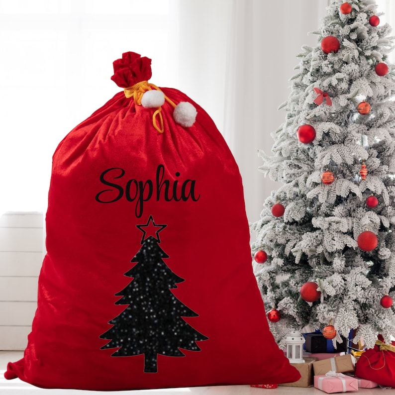 May include: A large red Christmas gift bag with the name "Sophia" in black script. A black Christmas tree design with a star and white accents is below the name. The bag is tied with a gold cord and white pom-poms.
