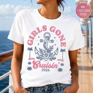 May include: A white short-sleeve t-shirt featuring a graphic design with the text "GIRLS GONE Cruisin' 2026". The design includes a blue anchor, palm trees, and floral elements, with the text in a distressed pink and blue font style.
