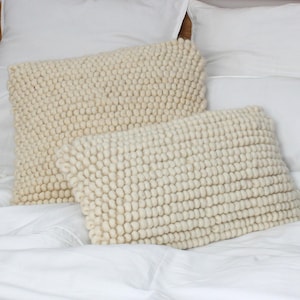 May include: A bed with white bedding and two cream-colored, textured pillows. The pillows have a nubby, raised surface. The headboard is made of light-colored wood. The bed is neatly made with crisp, white sheets and pillowcases.