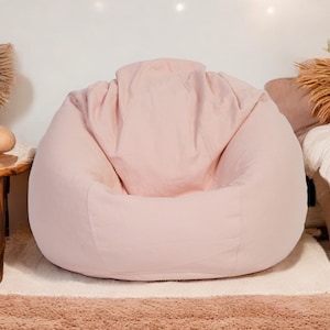 Könnte beinhalten: Ein hellrosa-farbener Sitzsack mit weichem, strukturiertem Stoff. Der Sitzsack steht auf einem hellbraunen Teppich.