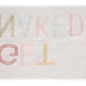 May include: A white bath mat with the words "naked" and "gel" embroidered in colorful thread.