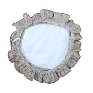 May include: A circular fabric cover featuring a white quilted center and a ruffled border with a mottled beige and reddish-brown pattern. The item has a gathered edge design and a soft, textured appearance, presenting a round shape overall.