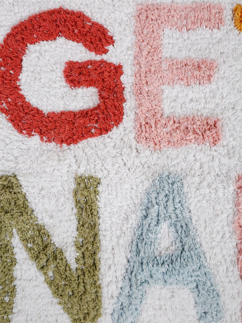 May include: A white bath rug with the word "GENA" spelled out in colorful, fluffy letters. The letters are red, pink, green, and blue.