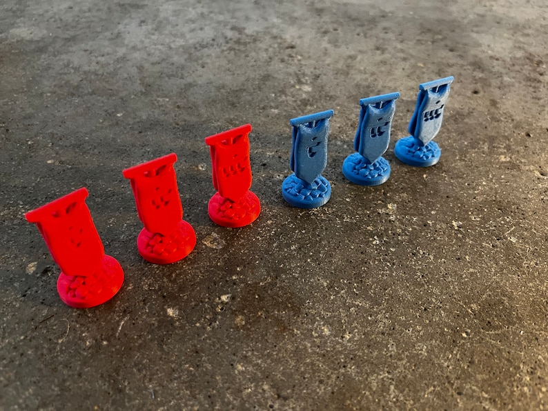 K&ouml;nnte beinhalten: Sieben Miniaturflaggen, drei rote und vier blaue, stehen auf einer grauen Oberfl&auml;che. Jede Flagge hat ein einzigartiges Design und ist auf einem kleinen Sockel montiert.