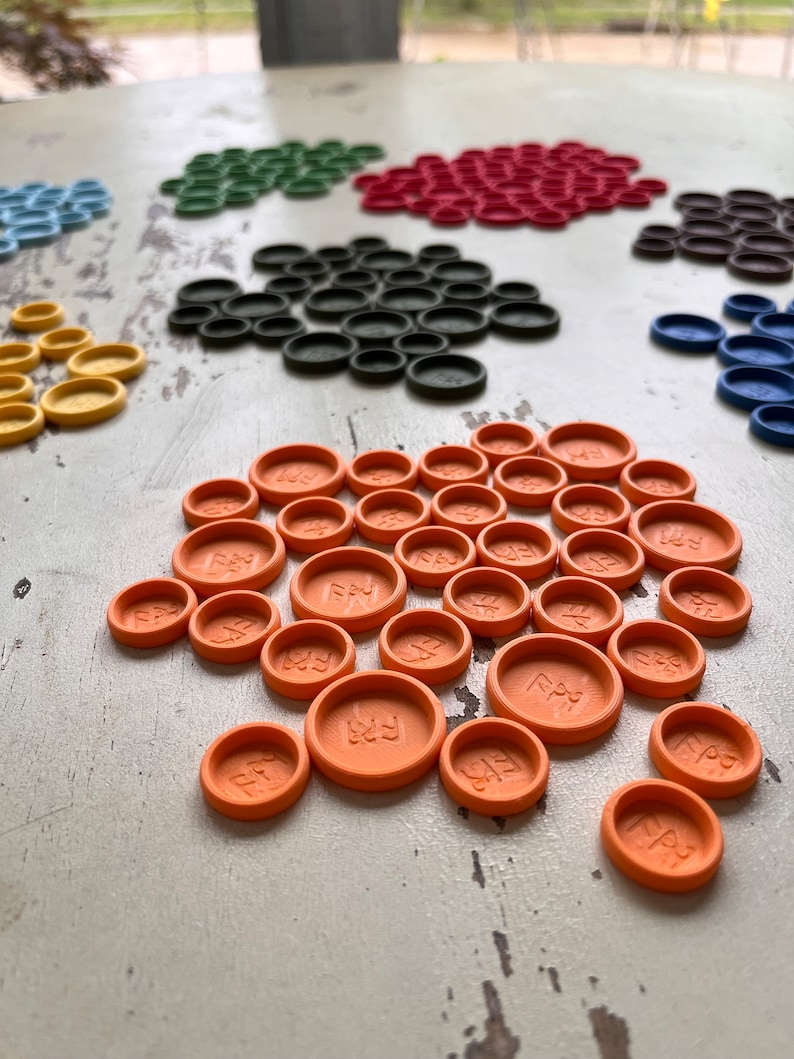 Puede incluir: Primer plano de un conjunto de fichas de juego de color naranja con la palabra "Play" inscrita en cada ficha. Las fichas est&aacute;n dispuestas en semic&iacute;rculo sobre una superficie de madera blanca.