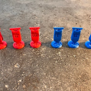 K&ouml;nnte beinhalten: Sechs Miniaturflaggen, drei rote und drei blaue, mit einem Symbol auf jeder Flagge. Die Flaggen befinden sich auf einer grauen Oberfl&auml;che.
