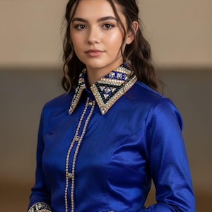 May include: A royal blue long-sleeve show shirt with a jeweled collar and cuffs. The collar and cuffs feature a geometric design with black, silver, and gold accents. The shirt has a button-down front with a jeweled embellishment. The Marrie Show Clothes logo is visible.