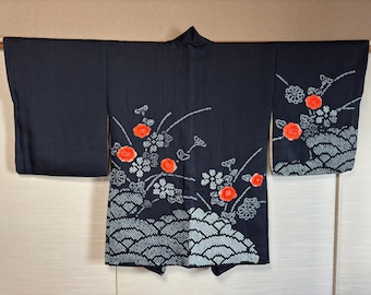 Op de afbeelding: Een donker marineblauwe kimono met een bloemenpatroon. Het ontwerp heeft oranje bloemen en grijze en witte bloemaccenten. De onderkant van de kimono heeft een golfachtig patroon in grijs en wit. De kimono wordt open getoond, met het volledige ontwerp.