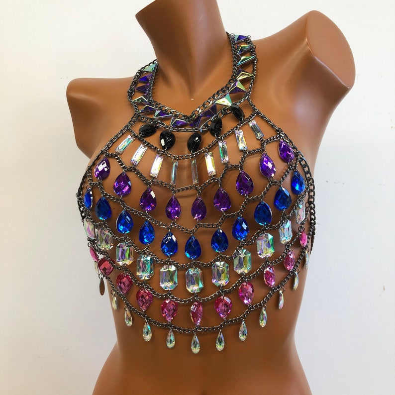 K&ouml;nnte beinhalten: Ein mehrlagiger, schillernder Kristall- und Ketten-K&ouml;rper-Schmuck. Der Schmuck besteht aus silbernen Ketten und verf&uuml;gt &uuml;ber rosa, blaue und violette Kristalle.