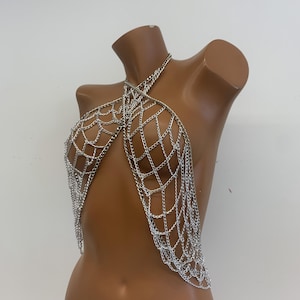 May include: Silver chain body jewelry with a web-like design. The chain is made of multiple strands and hangs down the front of the body.