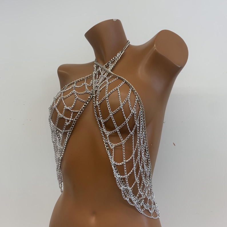 May include: Silver chain body jewelry with a web-like design. The chain is made of multiple strands and hangs down the front of the body.