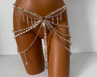 May include: A gold chain body jewelry piece with multiple strands of beads and dangling charms. The chain is adorned with clear and white beads, and the charms are made of gold and clear beads.