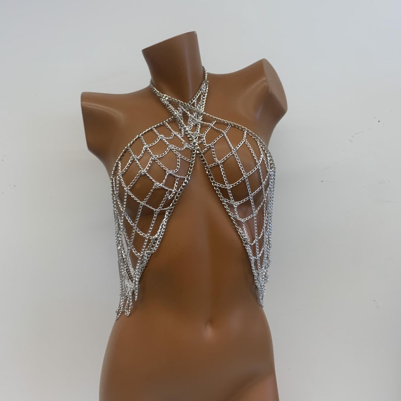 May include: Silver chainmail body jewelry with a criss-cross design. The chainmail is made of small, linked metal rings.