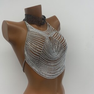 May include: Silver chainmail halter top with a black choker necklace. The top is made of interlocking metal rings and has a halter style neckline.