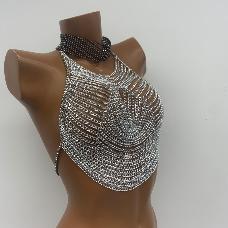 May include: Silver chainmail halter top with a black choker necklace. The top is made of interlocking metal rings and has a halter style neckline.