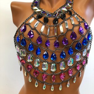 K&ouml;nnte beinhalten: Ein mehrlagiger Ketten-K&ouml;rper-Schmuck mit Tropfen- und rechteckigen Kristallen in den Farben Rosa, Blau, Lila und Irisierend. Die Kette ist silberfarben.