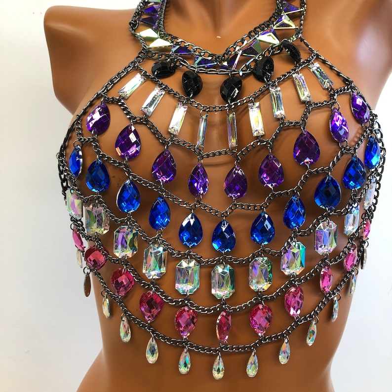 K&ouml;nnte beinhalten: Ein mehrlagiger Ketten-K&ouml;rper-Schmuck mit Tropfen- und rechteckigen Kristallen in den Farben Rosa, Blau, Lila und Irisierend. Die Kette ist silberfarben.