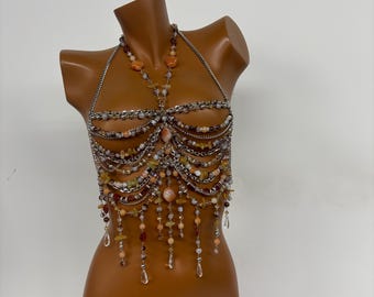 May include: A silver chainmail top with a halter neck design. The top is adorned with various earth-toned beads and dangling crystal-like pendants. The beads include shades of orange, brown, and green.