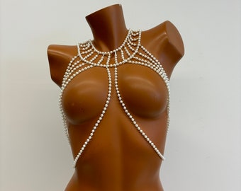 May include: A white pearl body chain with multiple strands forming a delicate and intricate design. The chain is worn on a mannequin, showcasing its fit and style.