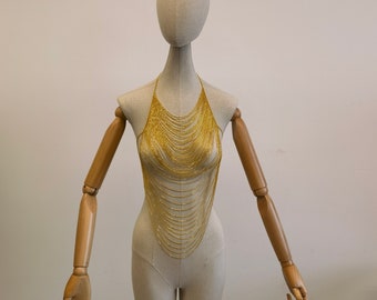 May include: A gold chain body jewellery piece on a mannequin. The chain is made of many small, thin gold chains that are layered on top of each other.