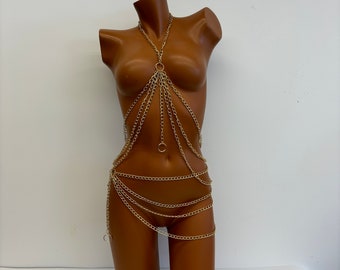 May include: Gold-colored body chain with multiple strands and circular accents. The chain drapes over the torso and hips of a mannequin. The body jewelry is designed to be worn as a fashion accessory.