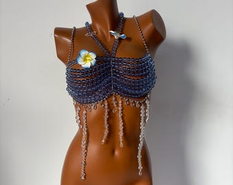 Può includere: Un top di reggiseno in perline blu con un accento di fiore bianco e una frangia di perline trasparenti.
