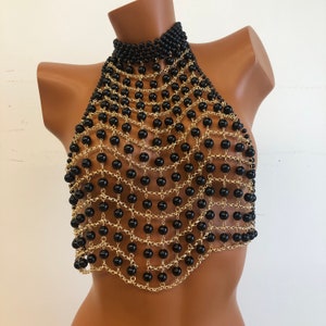 May include: A black and gold beaded halter top. The top is made of a chain with black beads attached to it. The chain is gold in color.