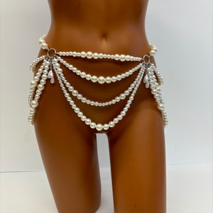 May include: A white pearl body chain with multiple strands and silver clasps. The chain is worn on a mannequin and features a dangling pearl design.