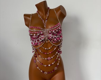 May include: A pink and white beaded bra top with gold chain accents. The bra top is layered with multiple strands of beads and chains, creating a cascading effect.