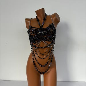 May include: A black beaded top with silver chain accents. The top is made of multiple layers of beads and chains, creating a cascading effect. The beads are black and silver, and the chains are silver.