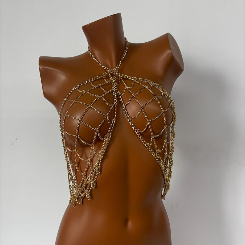 May include: A gold chain body jewelry piece with a web-like design. The chain is made of multiple strands of small, linked chains.