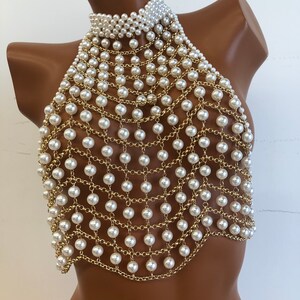 May include: A white pearl and gold chain halter top. The top is made of a delicate chain with white pearls attached to it. The top is designed to be worn as a halter top, with the chain going around the neck and the pearls hanging down the front of the body.