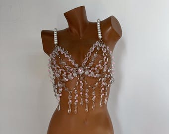 May include: A delicate beaded bra top with a pink and clear crystal design. The bra top features a crystal embellishment in the center and dangling crystals.